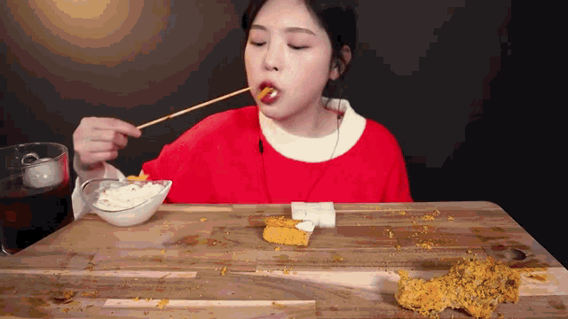 a woman in a red shirt is eating food with chopsticks on a table