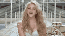 a woman in a white dress is sitting on a bench smiling .