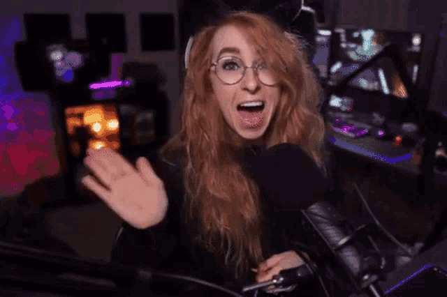 a woman with red hair and glasses is sitting in front of a microphone in a room .