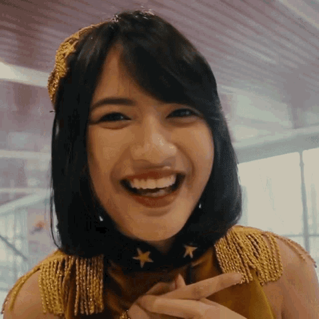 a woman wearing a gold outfit with stars on her neck smiles
