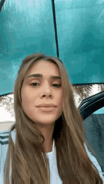 a woman is sitting in a car under an umbrella and looking at the camera .