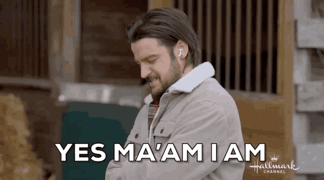 a man wearing ear buds is standing in front of a barn and says yes ma 'am i am .