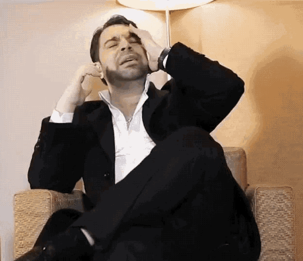 a man in a suit is sitting in a chair with his legs crossed and his head in his hands .