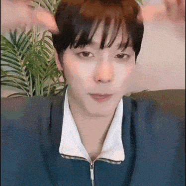 a young man in a blue jacket is sitting on a couch and making a funny face .