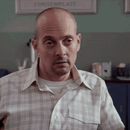 a bald man wearing a plaid shirt is making a funny face .