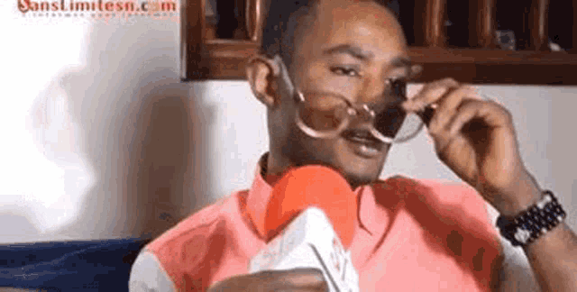 a man is wearing sunglasses and talking into a microphone while sitting on a couch .