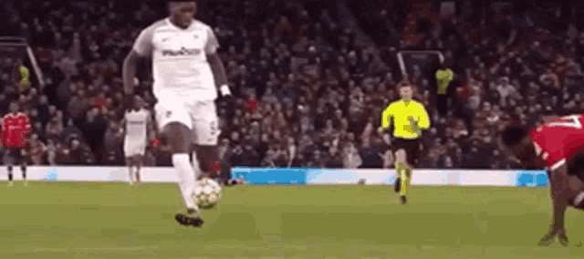 a soccer player is kicking a soccer ball on a field with a referee in the background .