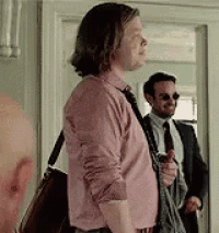 a man in a pink shirt is standing next to another man in a suit .