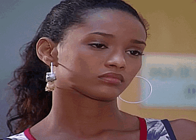 a woman wearing hoop earrings is looking at the camera with a serious look on her face .