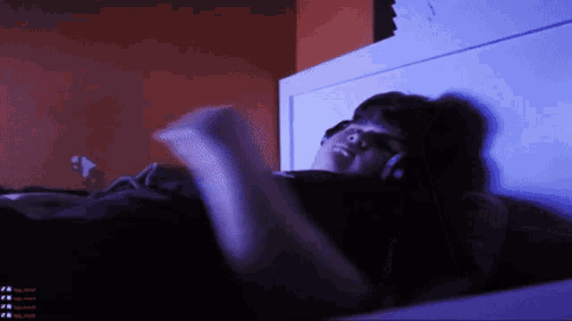 a person is laying on a bed with headphones on and a purple light behind them