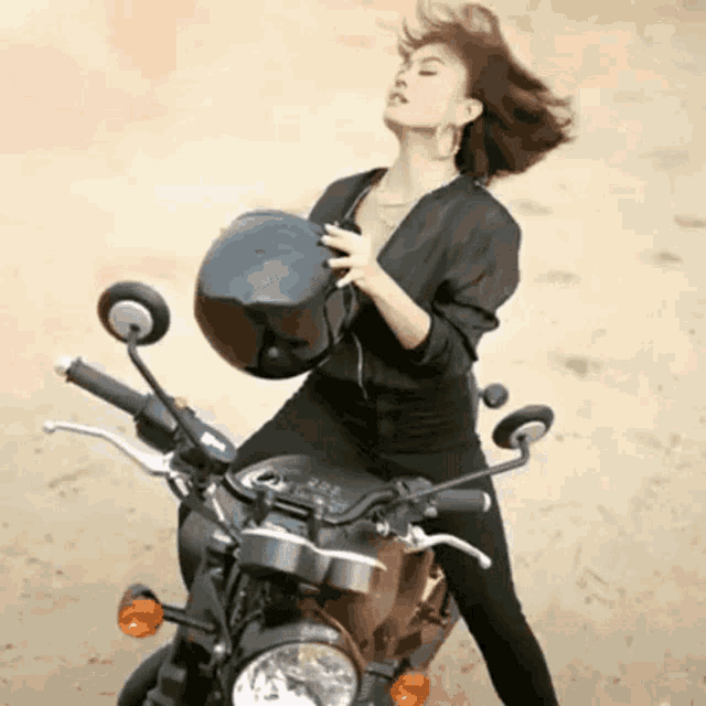 a woman is riding a motorcycle while holding her helmet