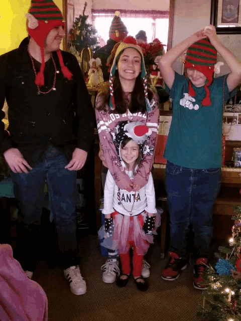 a girl wearing a santa shirt is being held by a man and two boys