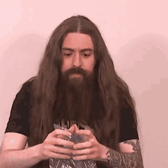 a man with long hair and a beard is holding a bottle in his hands .