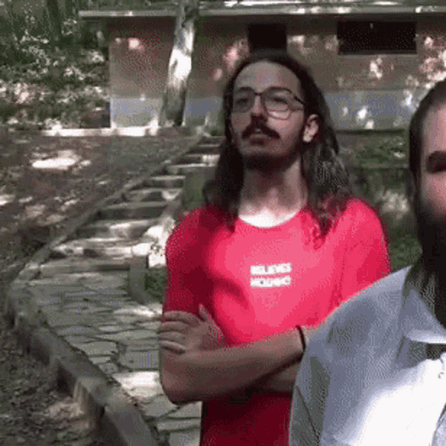 a man with long hair and glasses is wearing a red shirt that says believes in hounds