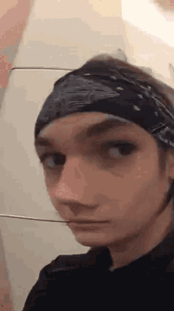 a young man wearing a bandana and a black shirt is making a face .