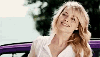 a woman is smiling in front of a purple car and looking at the camera .