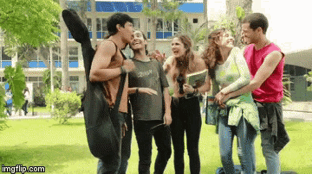 a group of young people standing in a park with a man carrying a guitar case ..