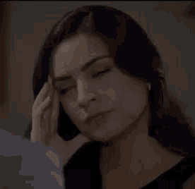 a woman is touching her face with her hand and looking at the camera .