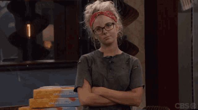 a woman wearing glasses and a red bandana is standing in front of a stack of pizza boxes .