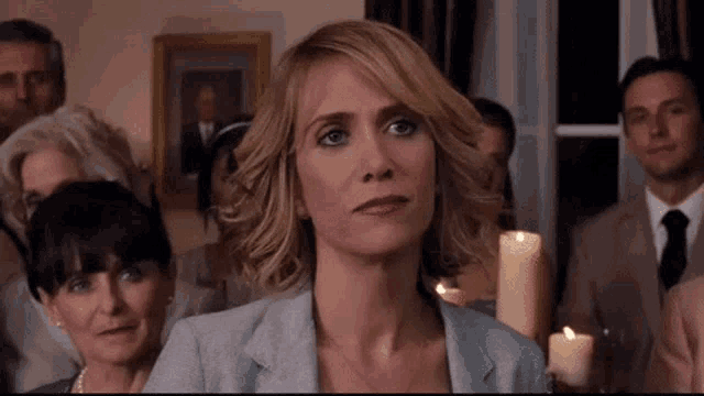 a woman in a suit is sitting in front of a group of people holding a candle .