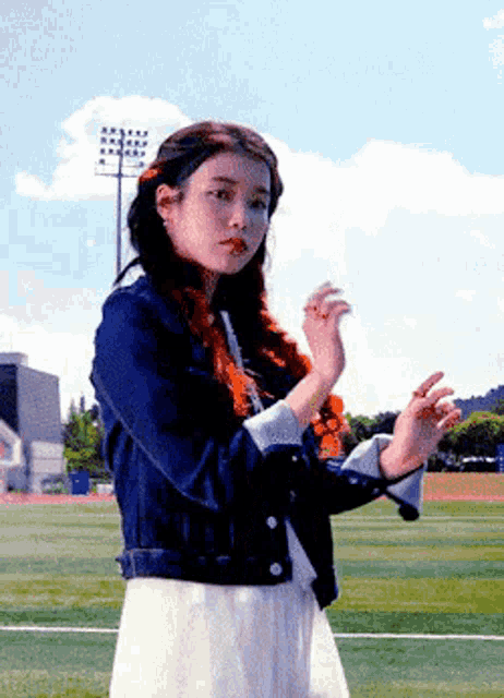 a girl in a white dress and a blue jacket stands on a field