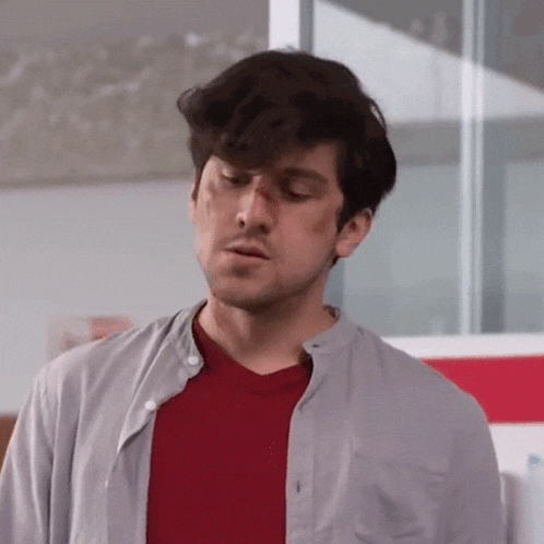 a man wearing a red shirt and a grey shirt has a scratch on his nose .