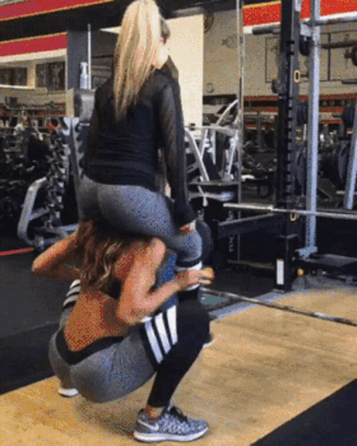a woman is squatting down carrying another woman on her back in a gym