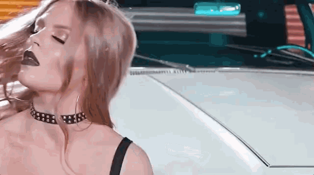 a woman in a choker is standing next to a white car .