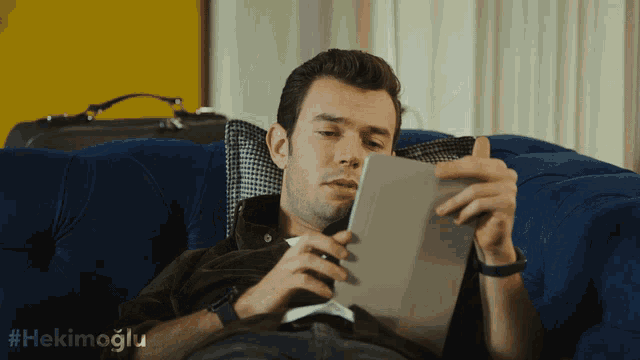 a man laying on a blue couch looking at a tablet with the hashtag #hekimoglu