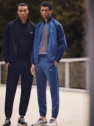 two men are standing next to each other on a bridge wearing blue tracksuits .