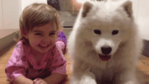 a little girl is laying on the floor next to a white dog