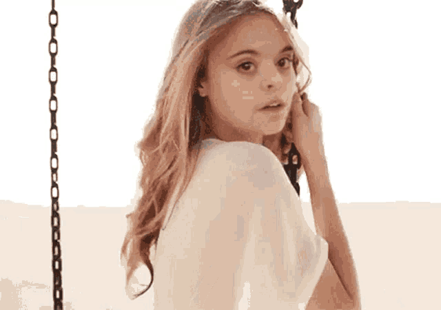 a young woman is sitting on a swing holding onto a chain .