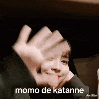 a person making a face with their hands and the words momo de katanne on the bottom right