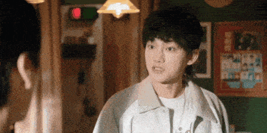 a young man with a mullet is standing next to a woman in a room and talking to her .
