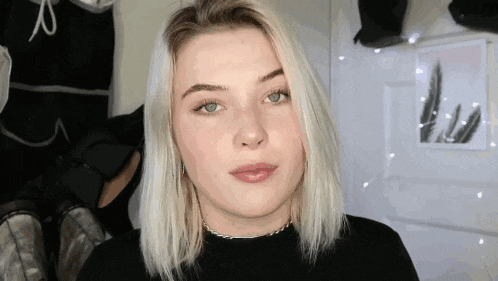 a woman with blonde hair and blue eyes is wearing a black shirt and looking at the camera .