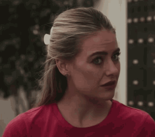 a woman wearing a red shirt and earrings looks to the side