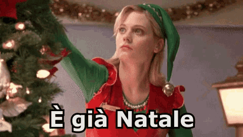 a woman dressed as an elf is decorating a christmas tree and the words e già natale are below her