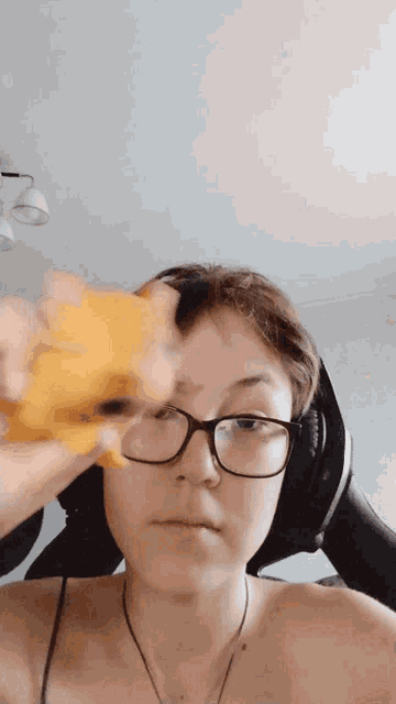 a woman wearing glasses and headphones holds a yellow object in front of her face .