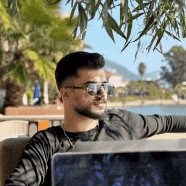 a man wearing sunglasses and a black shirt is sitting in front of a laptop