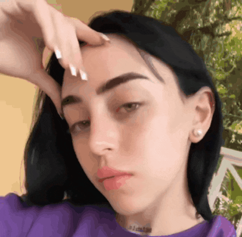 a woman in a purple shirt is touching her forehead with her hand