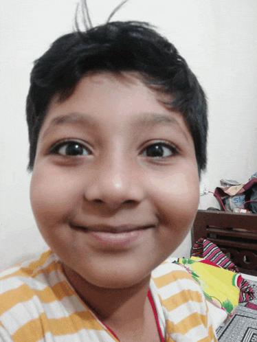 a young boy wearing a yellow and white striped shirt smiles