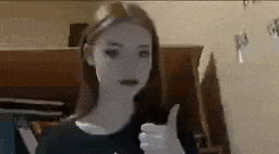 a woman is giving a thumbs up sign while standing in front of a piano .