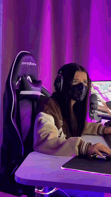 a woman wearing a mask and headphones is sitting at a desk with a computer .