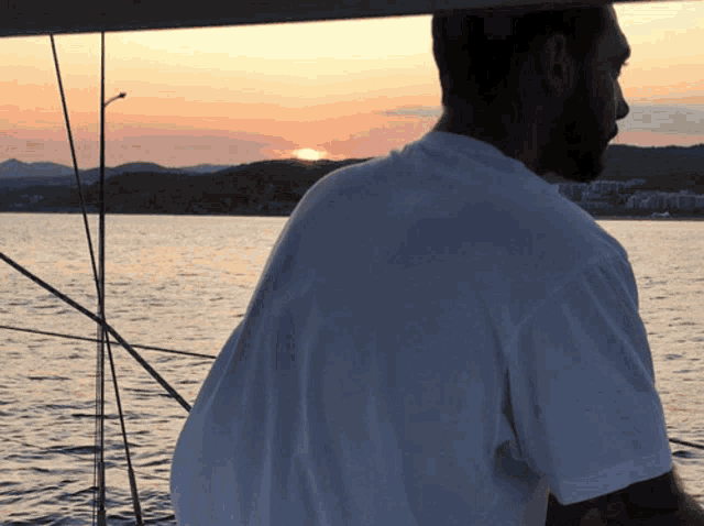 a man in a white shirt stands on a boat looking at the sunset