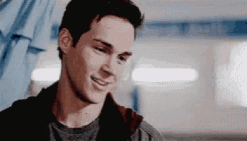 a young man is smiling and looking at the camera while standing in a hallway .
