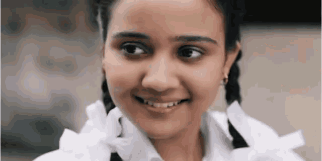 a young girl with pigtails and a white shirt smiles for the camera