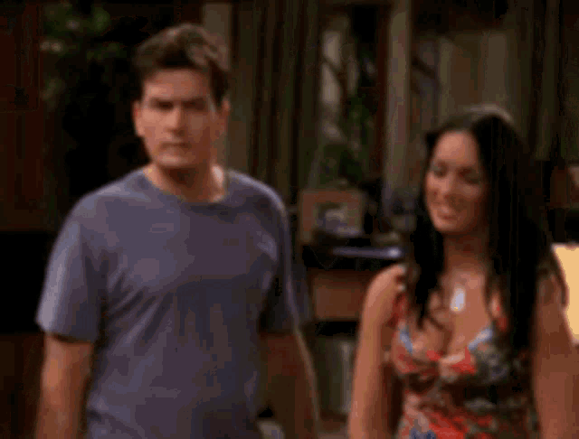 a man and a woman are standing next to each other in a living room and the woman is touching the man 's chest .