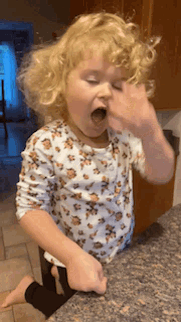 a little girl in a leopard print shirt is sitting on a counter with her mouth open