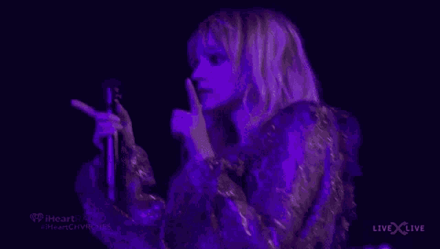 a woman is singing into a microphone while holding her finger to her mouth .