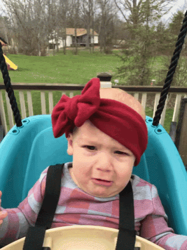 a baby wearing a red headband is crying in a blue swing